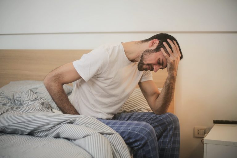 man-mental-fatigue-hearing-loss Man holds his head while sitting in bed.