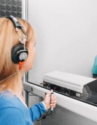 audiologist doing hearing exam to a mature patient using audiometer in special audio room.