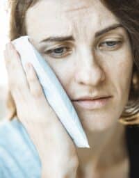 A woman holds an ice pack up to her face to relieve TMJ pressure.