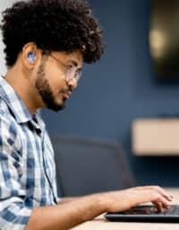 Side view of man wearing hearing aids working on laptop at office