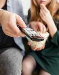 Couple watching TV and pointing remote.