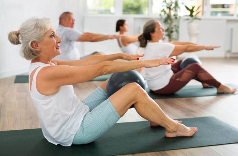 Portrait of senior people doing exercises for press with pilates ball during group class in fitness studio Woman using a medicine ball in yoga class