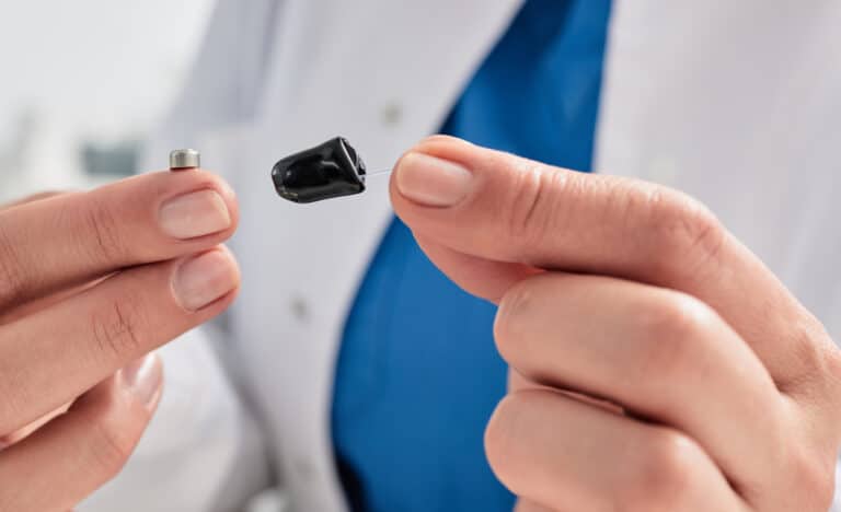 Hearing Aid Audiologist holding a small hearing aid and battery