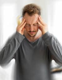Man with tinnitus holding his head, blurred effect around him