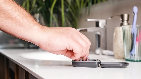 Close up of a hand grabbing hearing aids from their case.